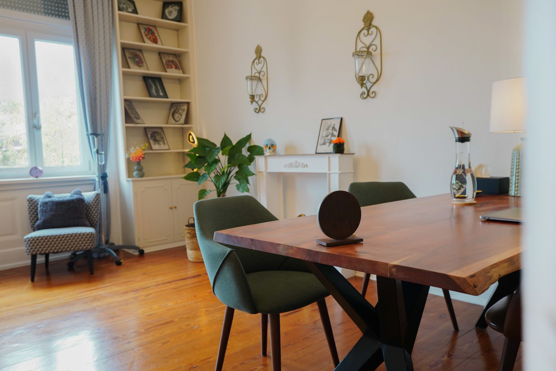 Heller Praxisraum mit Holztisch, grünen Stühlen und Bücherregal